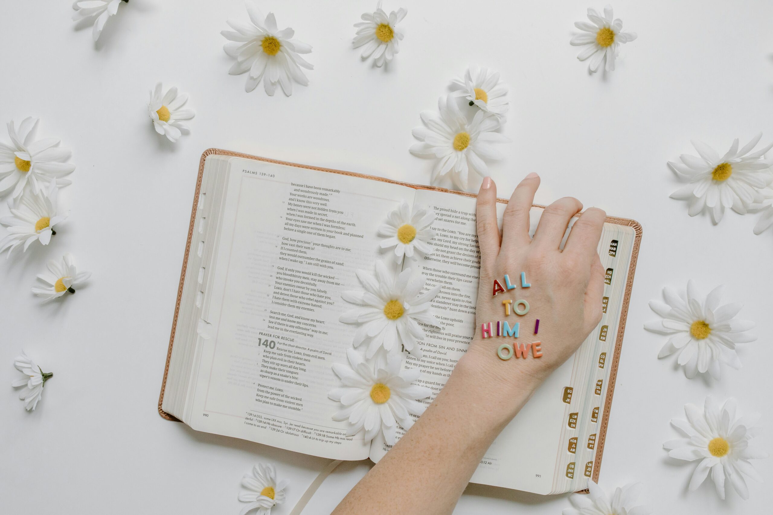 An open Bible surrounded by white daisies, with a hand displaying the phrase 'All to Him I Owe,' symbolizing faith, devotion, and spiritual renewal - Grace Online Church.